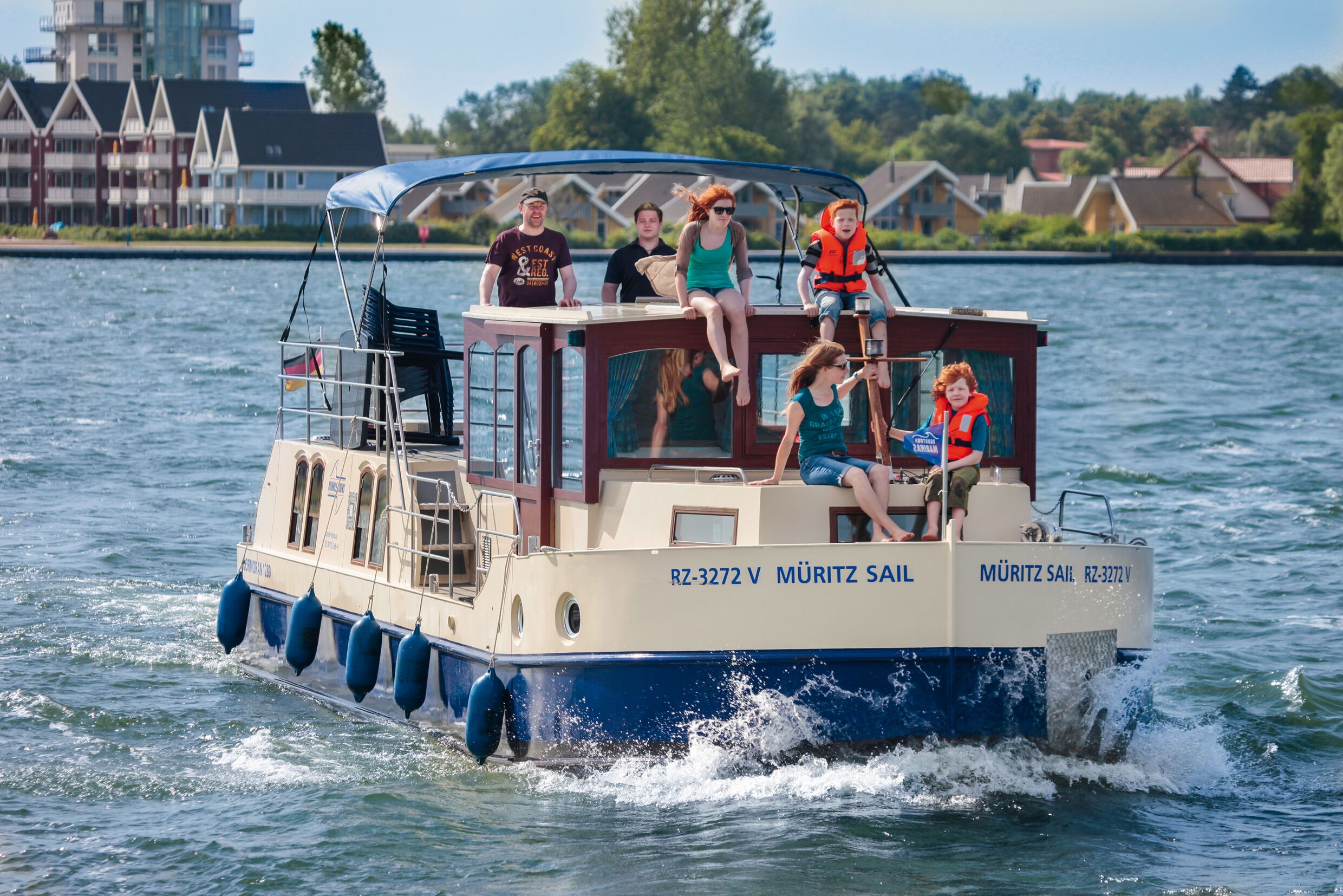 Un bateau avec des personnes à bord, une cabine dotée de fenêtres et une décoration aux couleurs bleu et blanc.