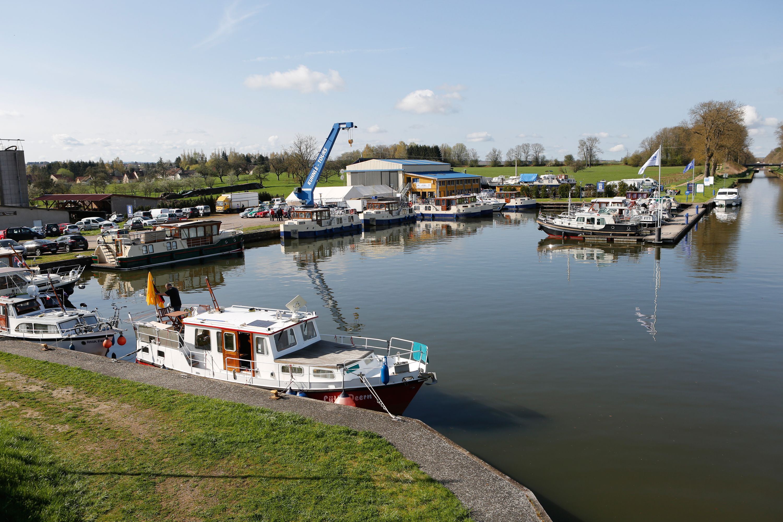 A marina with boats docked, a crane, and a building with a blue roof.