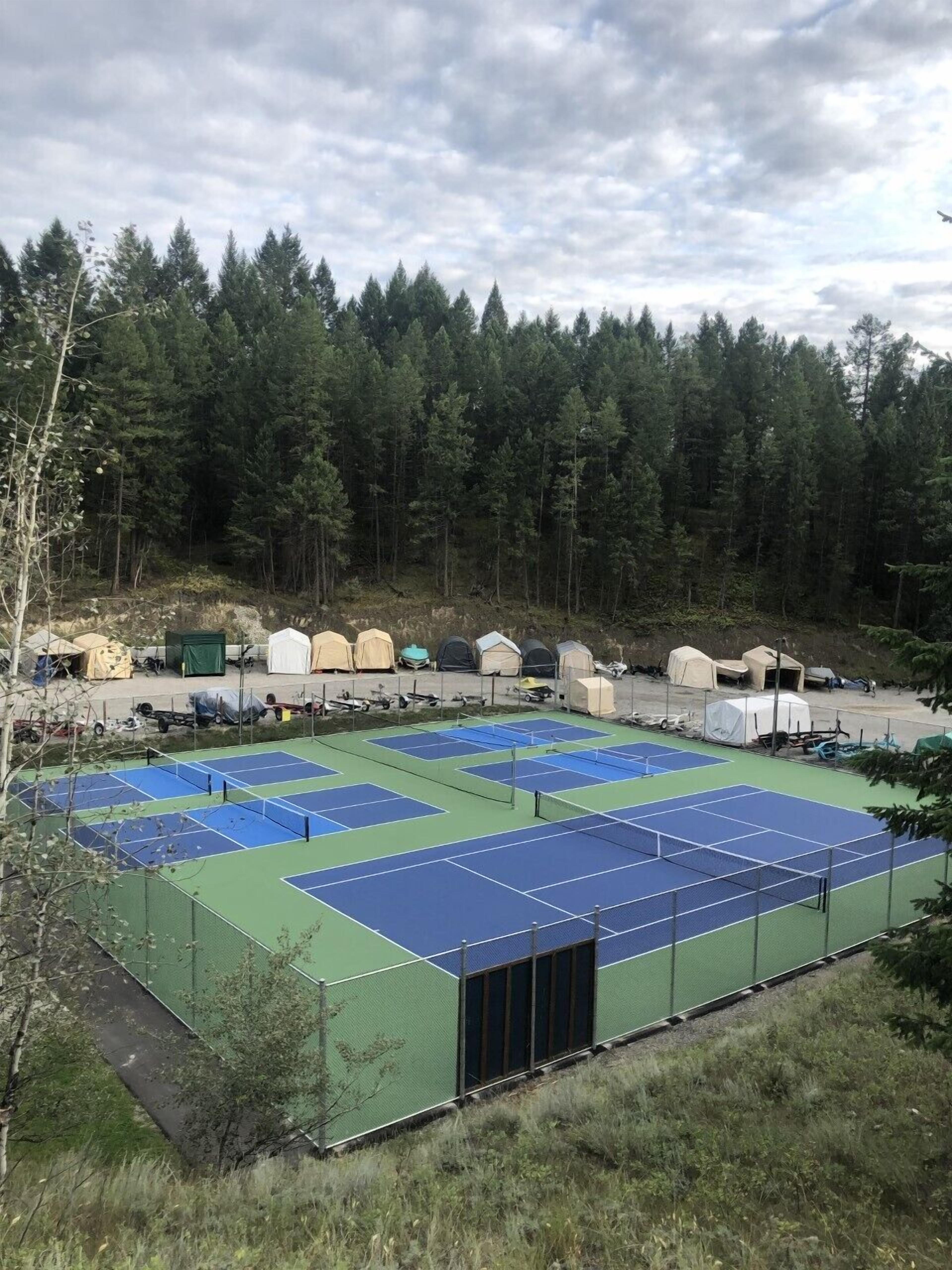 Een tenniscomplex met meerdere velden, omgeven door een bebost gebied en tenten.