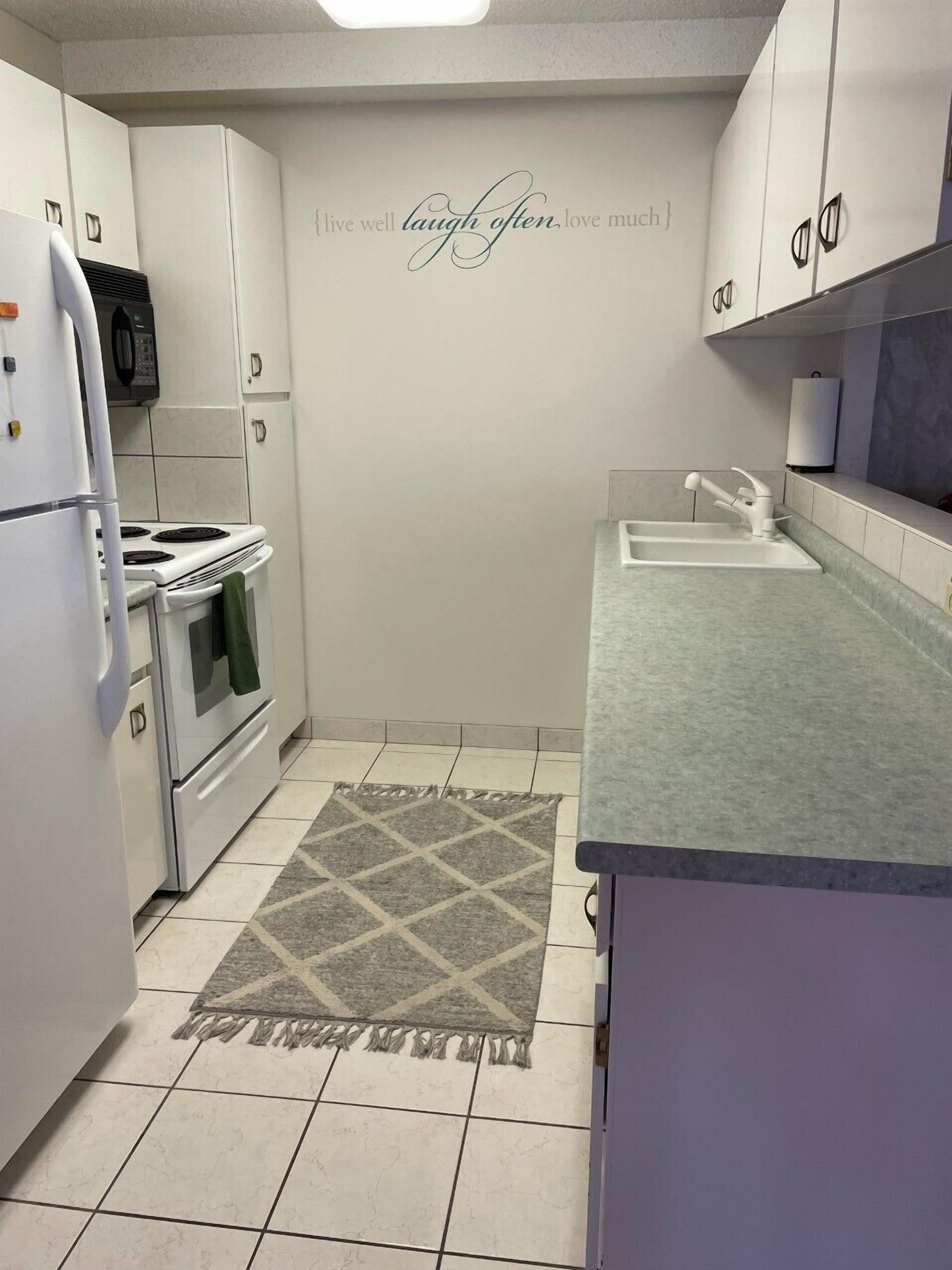 A compact kitchen with white cabinets, a microwave, a stove, and a sink. A decorative rug is on the floor.