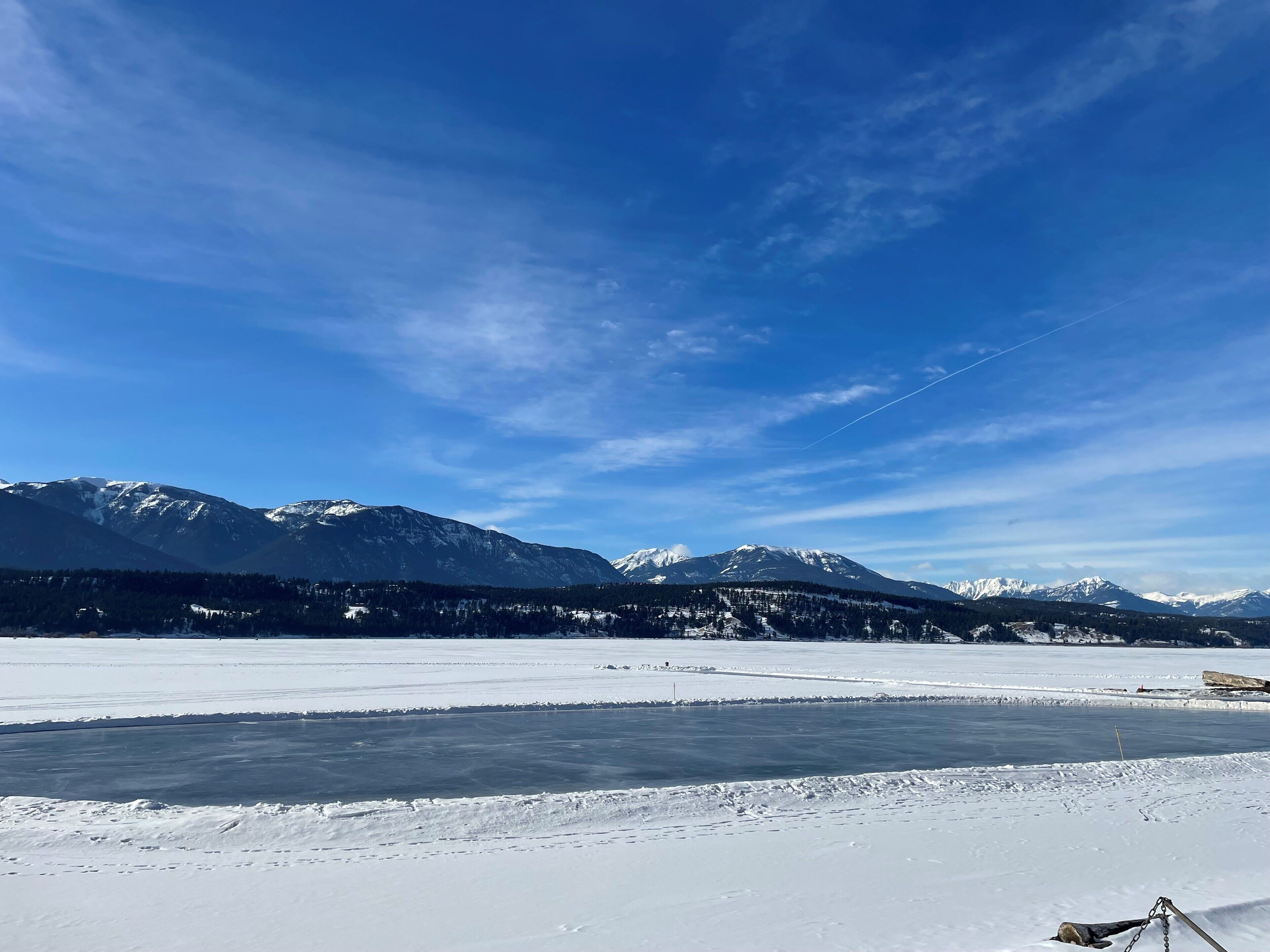 A snowy landscape with mountains in the background and a frozen body of water in the foreground.