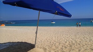 Una playa con una sombrilla azul, arena y el océano al fondo.