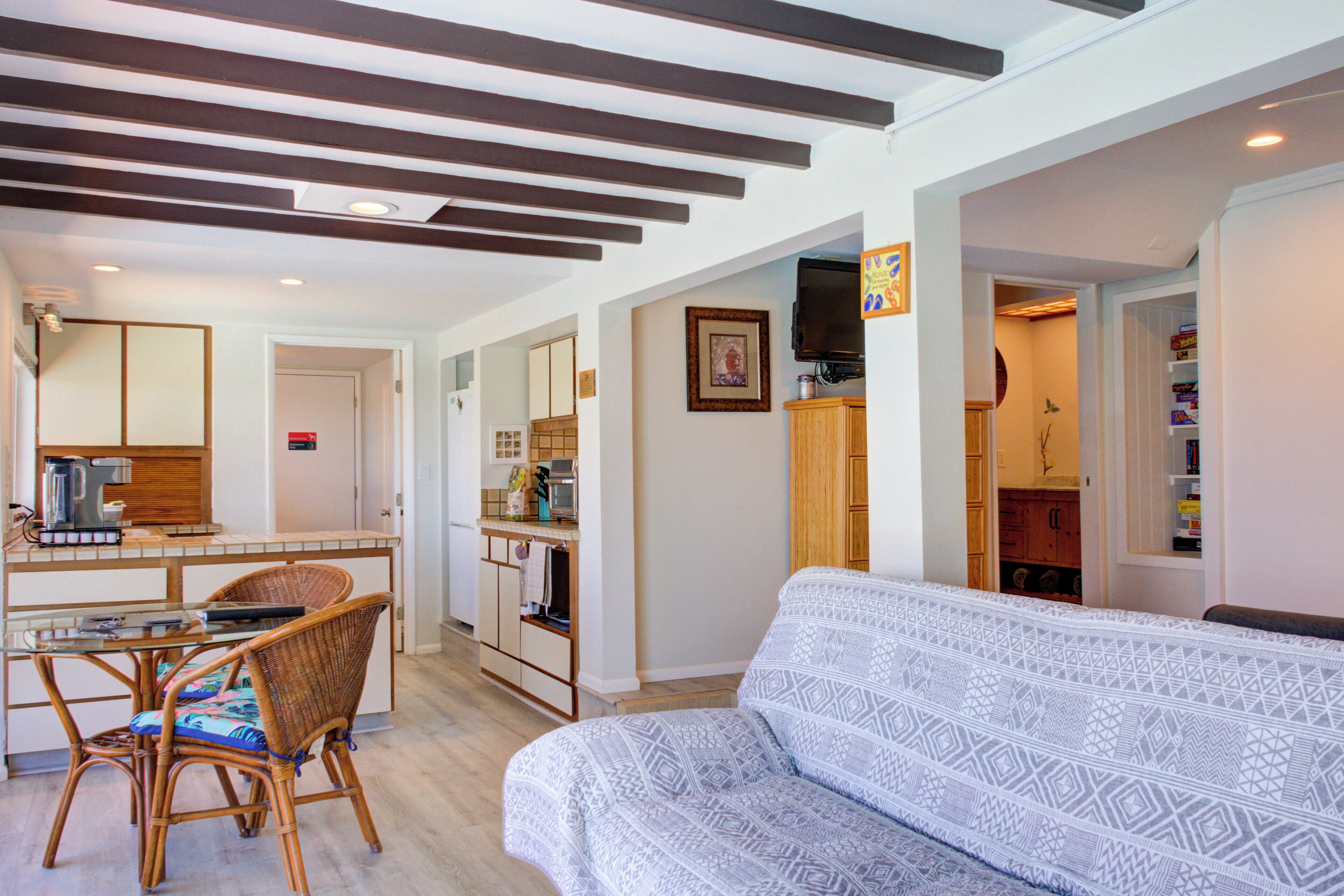 A living room with a patterned sofa, a dining area with wicker chairs, and a kitchen with wooden cabinets.