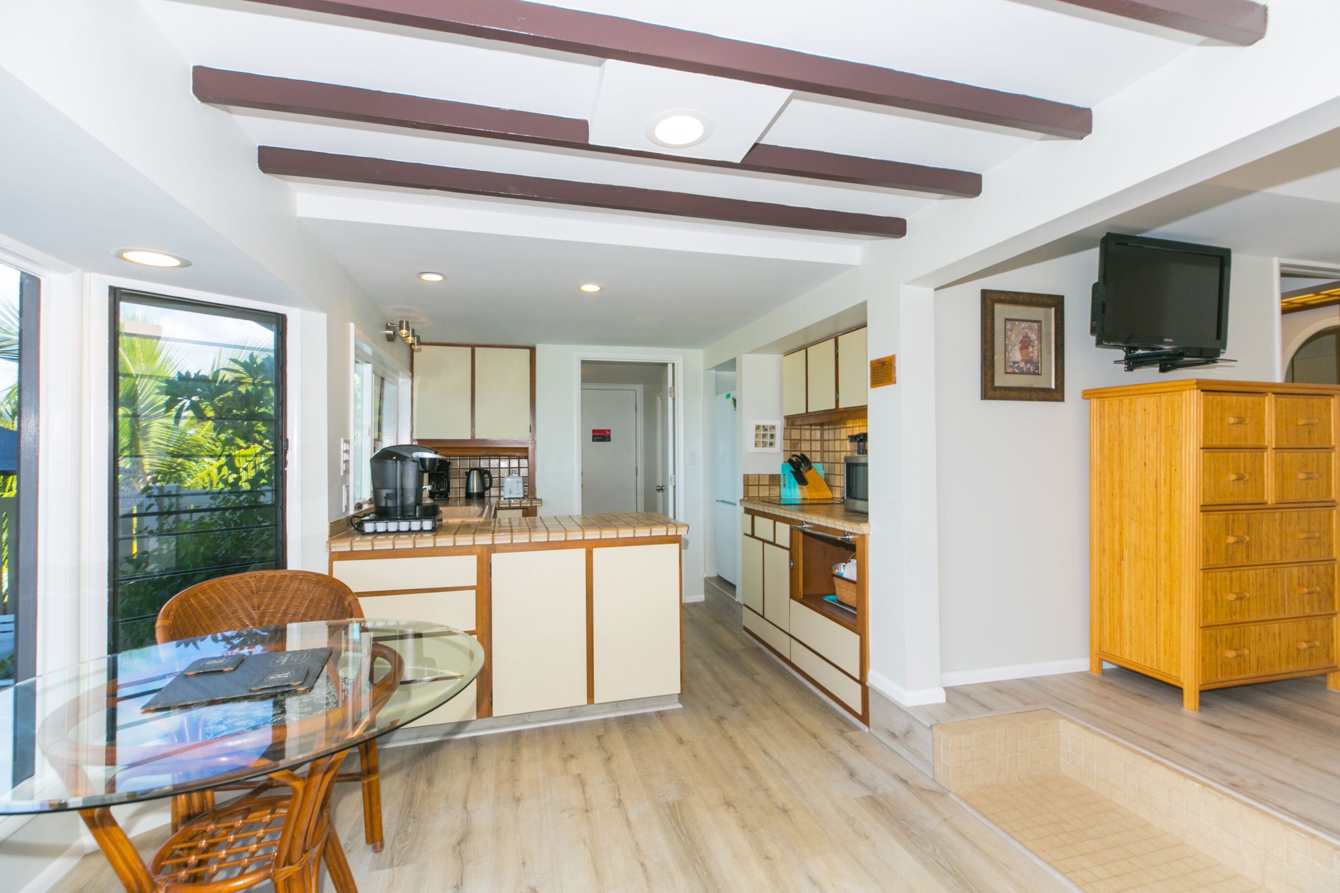 A modern kitchen with a glass dining table, wooden cabinets, and a built-in TV.