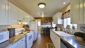 A kitchen with white cabinets, a stove, a sink, and a dining area with chairs and a table. - Shasta Star. Mountain views in downtown Mt. Shasta (Mt Shasta)