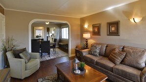 A living room with a brown leather sofa, a beige armchair, and a wooden coffee table. There is a dining area with a table and chairs in the background. - Shasta Star. Mountain views in downtown Mt. Shasta (Mt Shasta)