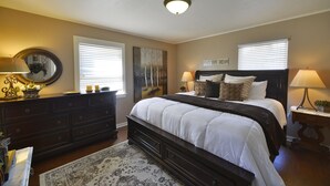 A bedroom with a large bed, dark wooden dresser, two bedside tables with lamps, a round mirror, and a painting on the wall. - Shasta Star. Mountain views in downtown Mt. Shasta (Mt Shasta)