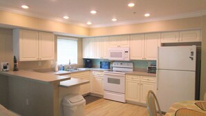 Una cocina compacta con armarios blancos, un microondas, una estufa y un refrigerador.