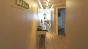 Un pasillo estrecho con suelo de madera, una mesita con una cesta y una puerta que da a una habitación con un aparador.