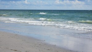 Una playa con olas acercándose a la orilla, un cielo despejado y un horizonte lejano.