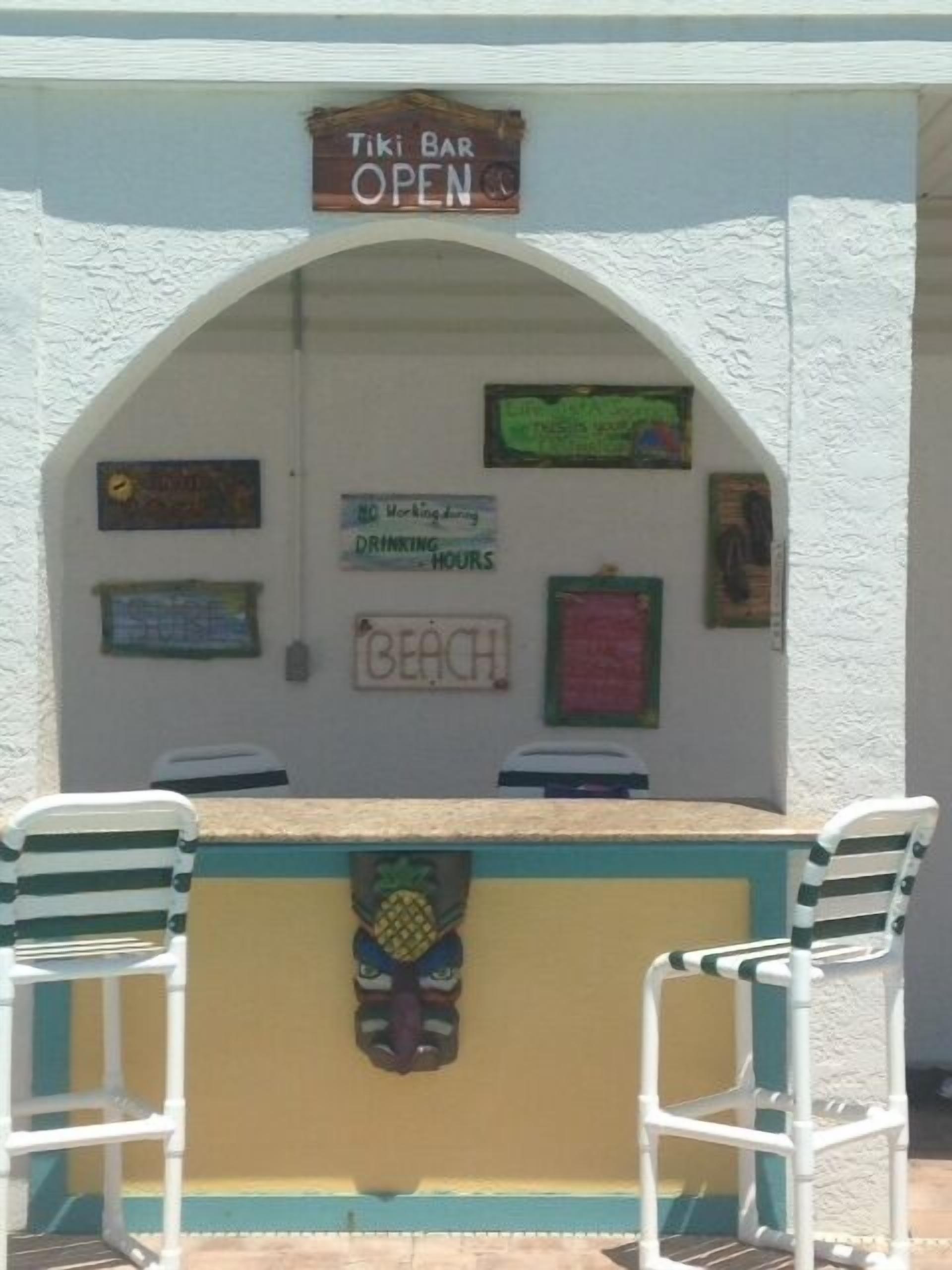 A tiki bar with a sign indicating it is open. There are two chairs in front of the bar.