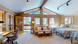 A cozy cabin with a loft bedroom, a study area with a desk and chair, and a large window providing a view of the outdoors.