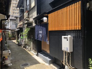 Une ruelle étroite, bordée de bâtiments des deux côtés, avec une clôture en bois et une enseigne portant des caractères japonais.