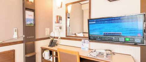A hotel room with a bed, a desk with a computer, a telephone, a mirror, and a clock on the wall.