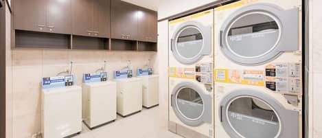A laundry facility with four washing machines and three dryers, each with control panels and instructions.