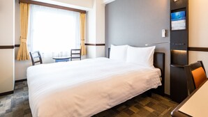 Habitación de hotel con una cama grande, una mesita, dos sillas, una ventana con cortinas y un televisor montado en la pared.