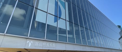 A modern building with large glass windows and a sign indicating it is the Toyama Prefectural Museum of Art and Ethnography.