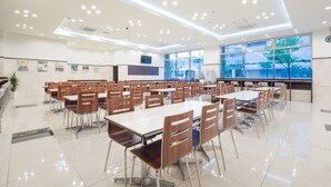 Una amplia cafetería con numerosas mesas y sillas, ventanas grandes y un diseño moderno en el techo.