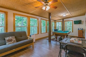 A room with a sofa, pool table, and a ceiling fan.