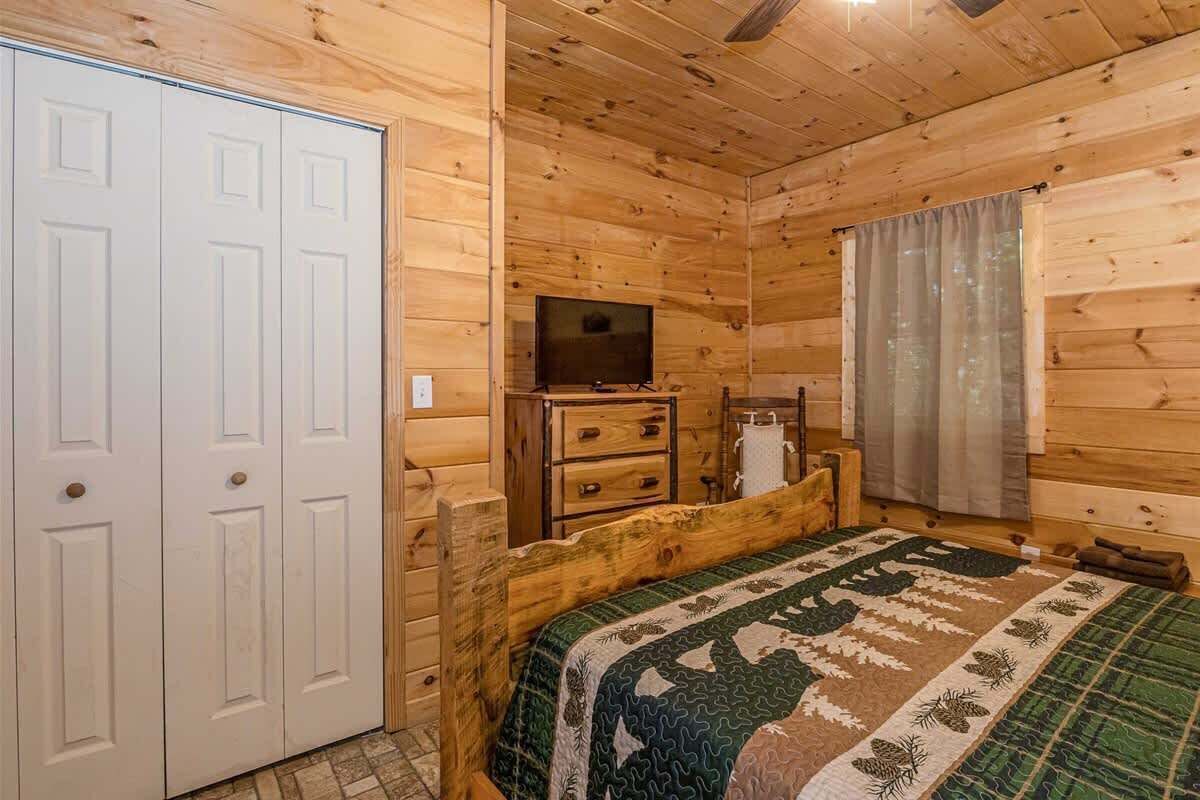 A wooden cabin bedroom with a bed, a TV, a dresser, and a closet.