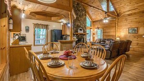 Interior de uma cabana de madeira com uma mesa de jantar posta para quatro pessoas, lareira e sala de estar com sofá.