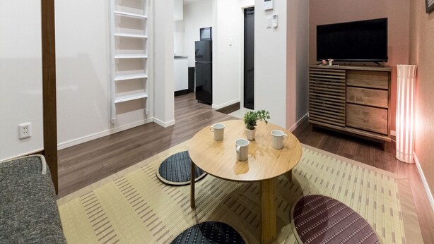 A compact living space with a dining area, a built-in TV, and a kitchen in the background. - Trip Pod Sumiyoshi A (Fukuoka)