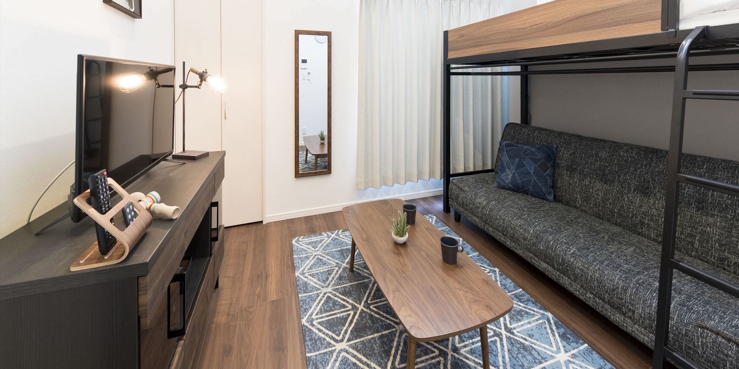 A compact room with a bunk bed, a desk with a lamp, a small table, and a sofa.
