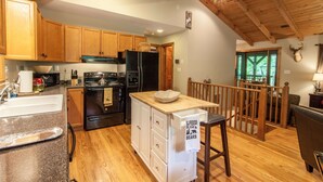 A kitchen with wooden cabinets, a black refrigerator, a stove, and a wooden dining area. - Cabin By Blue Ridge Parkway (Blowing Rock)