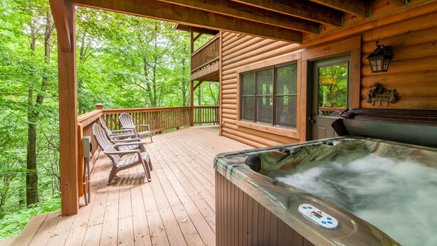 A wooden deck with Adirondack chairs, a hot tub, and a view of a forested area. - Cabin By Blue Ridge Parkway (Blowing Rock)