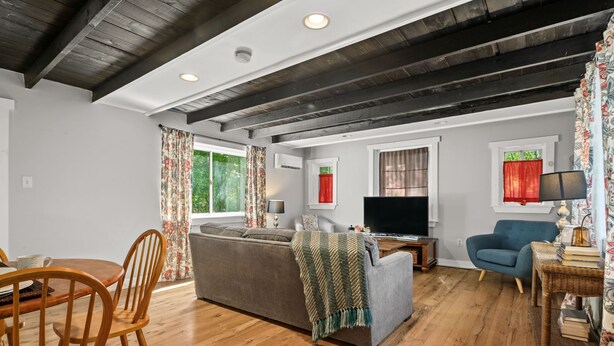 A modern living room with a wooden ceiling, a grey sofa, a blue armchair, and a dining area with wooden chairs and a table. - Cottage w/ Private Fenced Yard | Dogs OK (Wilmington)