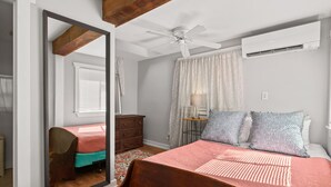 A bedroom with a wooden bed, a ceiling fan, an air conditioning unit, a mirror, a dresser, and a window with curtains. - Cottage w/ Private Fenced Yard | Dogs OK (Wilmington)