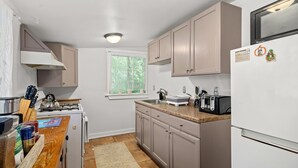 A compact kitchen with a gas stove, microwave, and a refrigerator. There is a window providing natural light, and the kitchen features light-colored cabinets and a wooden countertop. - Cottage w/ Private Fenced Yard | Dogs OK (Wilmington)