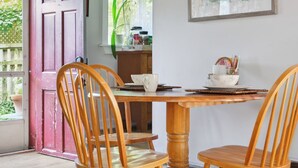 A dining area with a wooden table and chairs, a framed artwork on the wall, and a red door leading outside. - Cottage w/ Private Fenced Yard | Dogs OK (Wilmington)