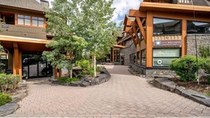 A building with a stone facade and wooden accents, a sign for 'One Wellness', and a paved walkway with landscaping. - Mökki Mountain Suite - mountain views & private corner unit (Canmore)