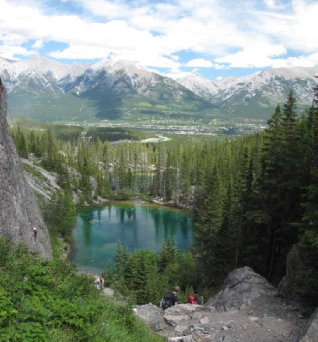 A mountainous landscape with a lake surrounded by dense forest and distant peaks.