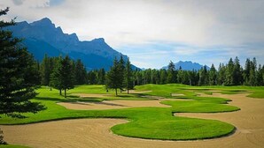A golf course with sand bunkers, trees, and mountains in the background. - Mökki Mountain Suite - mountain views & private corner unit (Canmore)