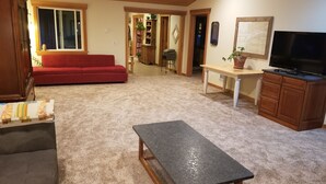 Una sala de estar con un sofá rojo, una mesa gris oscuro, armarios de madera y un televisor.