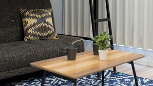 A modern living room with a grey sofa, a patterned throw pillow, a small wooden table with a plant and a black mug, and a blue patterned rug. - Trip Pod Sumiyoshi C (Fukuoka)