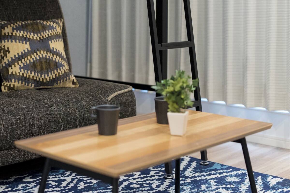 A modern living room with a grey sofa, a patterned throw pillow, a small wooden table with a plant and a black mug, and a blue patterned rug.