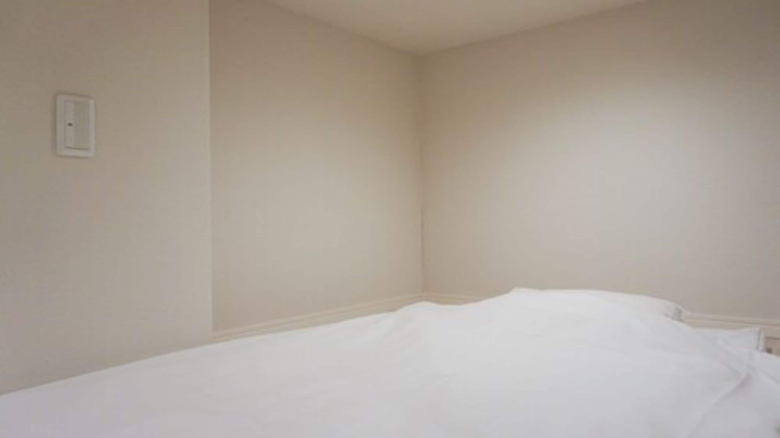 A small, unadorned room with a single bed and a light switch on the wall.