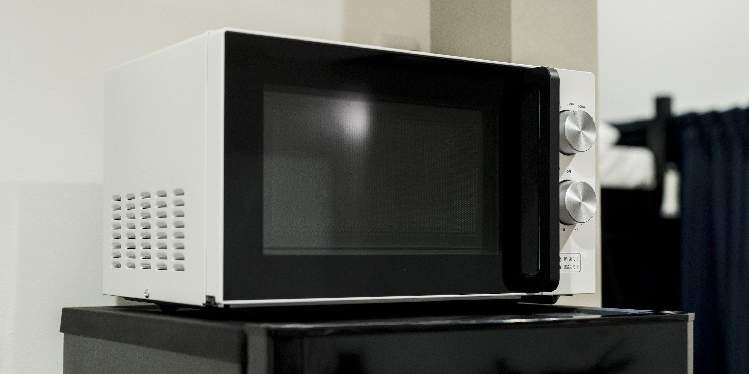 Un microondas sobre un electrodoméstico negro, posiblemente un refrigerador, con un panel de control en el lado derecho.