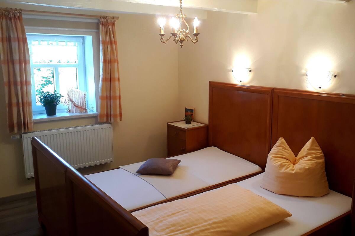 A double bed with a wooden headboard, a bedside table with a lamp, and a window with curtains.