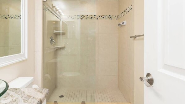 Un baño con ducha de vidrio, inodoro y lavamanos con encimera de mármol.