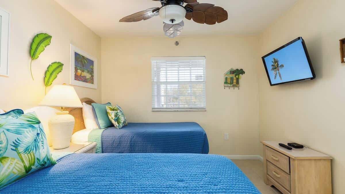 Camera da letto con due letti, una ventola a soffitto, una finestra, una TV e un comodino.