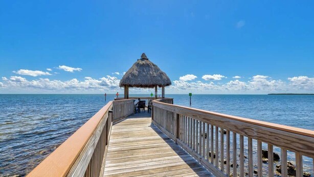 A wooden pier leading to a thatched-roof structure with a view of calm waters and a clear sky. - Sunrise Suite with Unobstructed Ocean Views (Tavernier)
