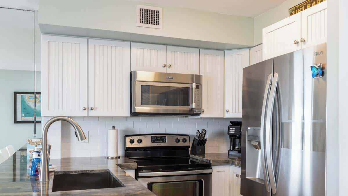 A modern kitchen with white cabinets, stainless steel appliances including a microwave, stove, and refrigerator, and a built-in sink.