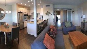 A modern living room with a sofa, coffee table, and TV. A kitchen with white cabinets and a dining area with a table and chairs are visible. - Adorable waterfront condo, private docks, and bring the dog! (Horseshoe Bay)