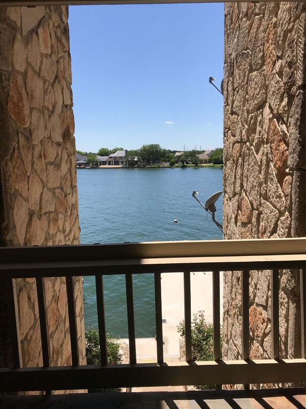 A stone balcony with a view of a lake, a bird feeder, and a distant house. - Adorable waterfront condo, private docks, and bring the dog! (Horseshoe Bay)