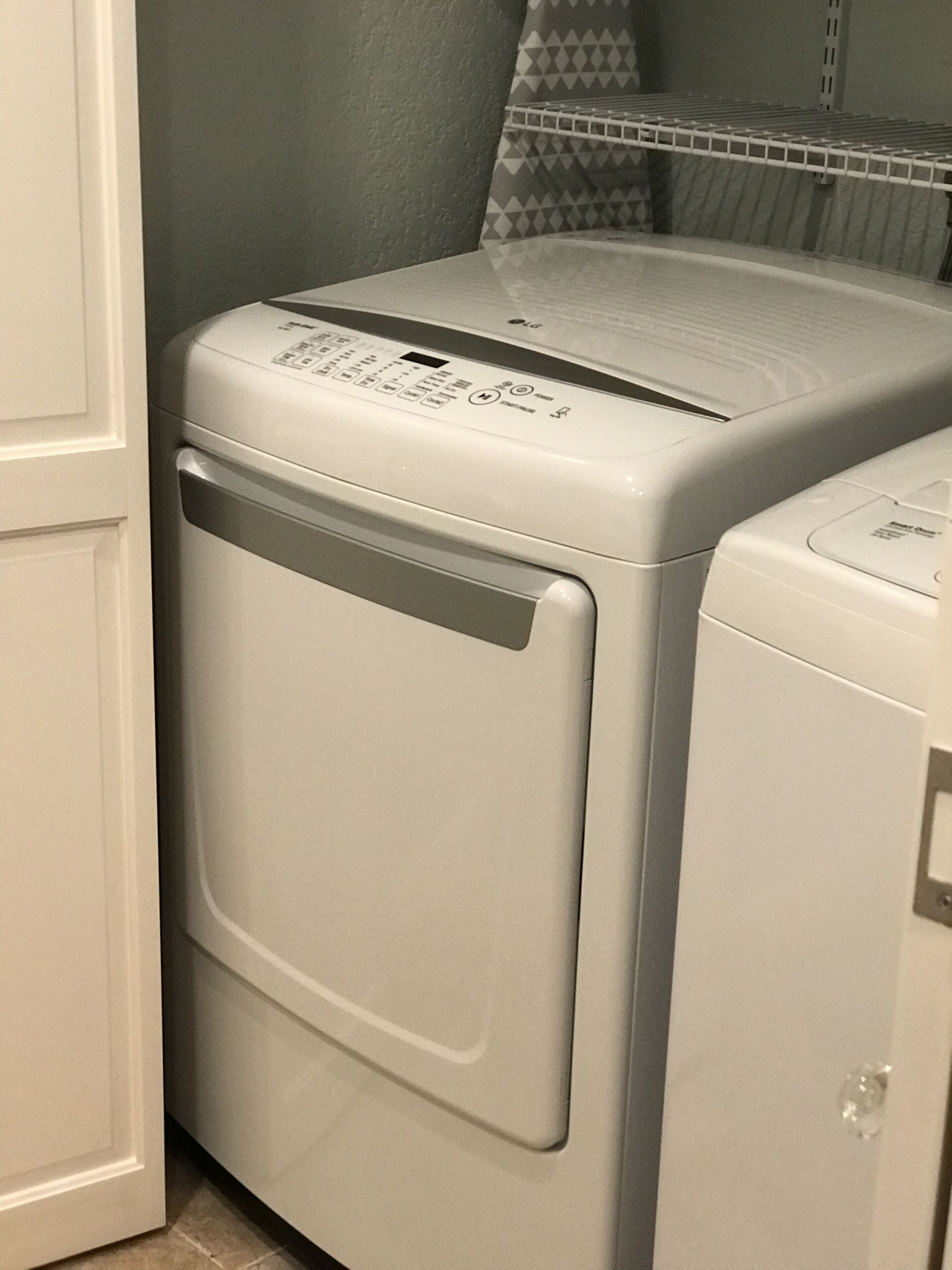 A front-loading white washer and dryer in a laundry room with a gray wall and patterned towel rack.