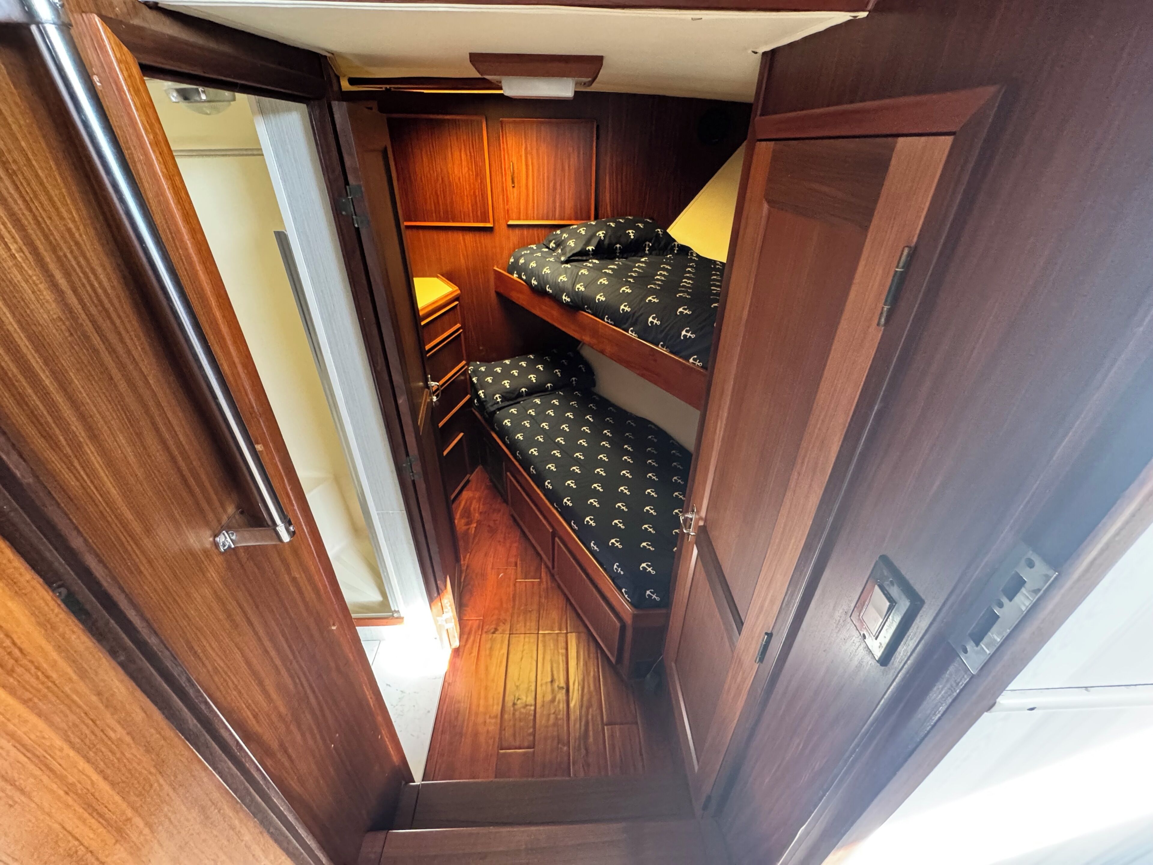 A narrow corridor leading to a compact bedroom with two bunk beds, a small bedside table, and a wardrobe.